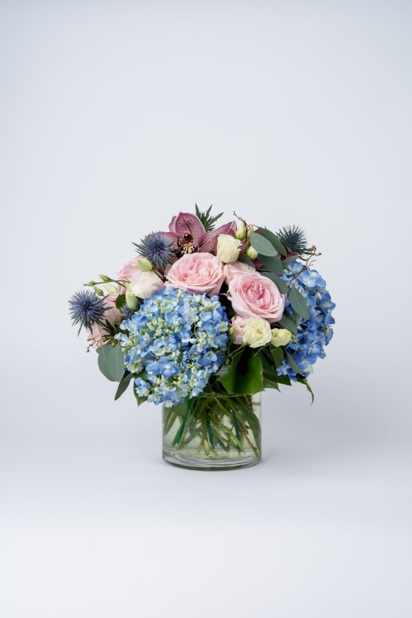 blue and pink flower arrangement. Blue hydrangeas, pink roses, orchids, and thistle in glass vase floral arrangement