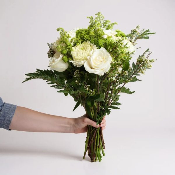 Hand holding white and green bouquet with roses, chrysanthemums, and greenery
