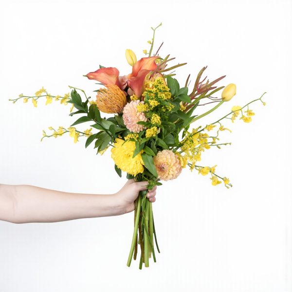 Hand holding bright bouquet with yellow tulips, peach dahlias, calla lilies, and orchids against white background