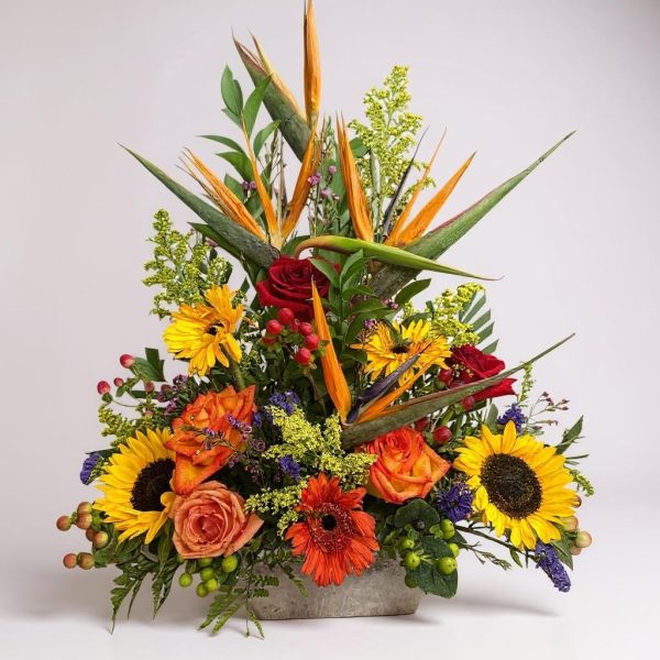 tropical flower arrangement with bird of paradise, sunflowers, roses, and gerbera in stone container