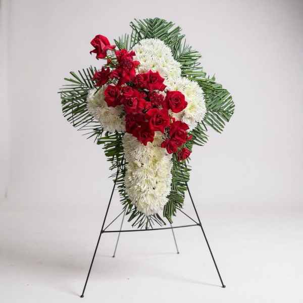 Funeral cross spray with white chrysanthemums, red roses, and greenery on easel