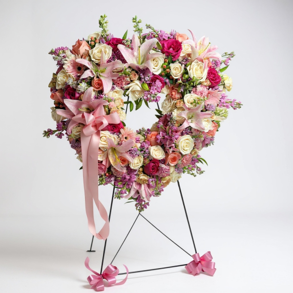 Funeral heart wreath with pink lilies, roses, gerbera daisies, and mixed pastel flowers with pink ribbon bow