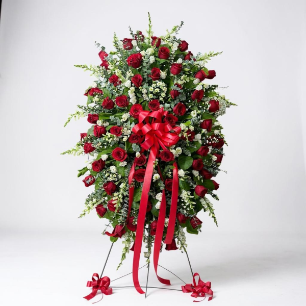 Funeral standing spray with red roses, white accent flowers, greenery, and red ribbon bow