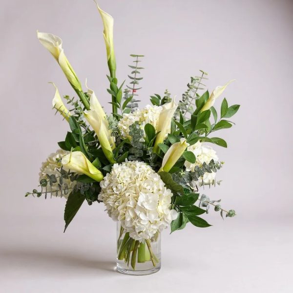 Elegant white calla lilies and hydrangeas arranged in a clear glass vase with eucalyptus and greenery