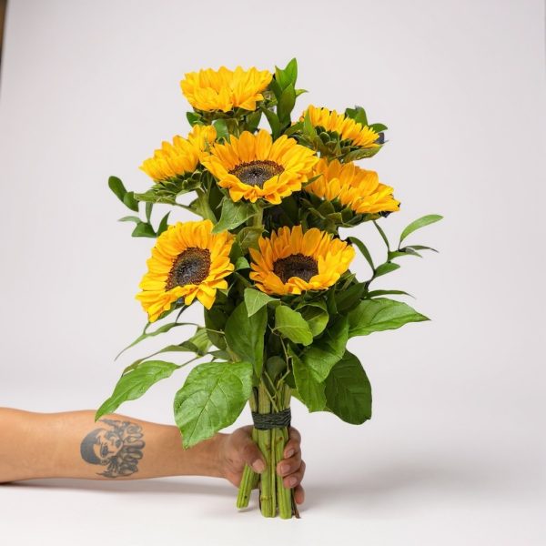 Hand holding a bouquet of sunflowers with bright yellow petals and greenery