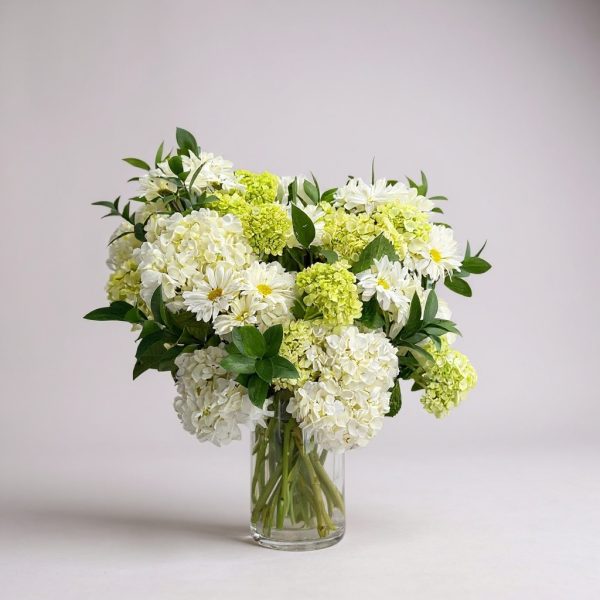 White and green flower arrangement in a clear vase with daisies and hydrangeas