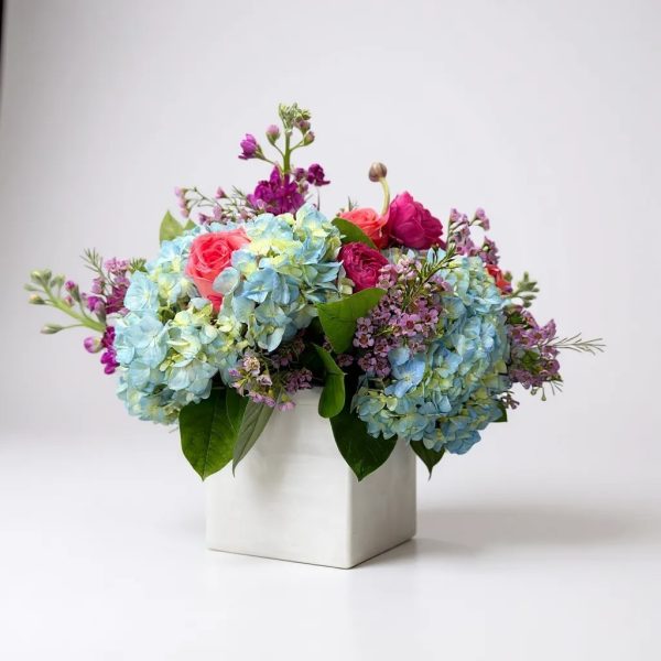 Garden Serenade flower arrangement with blue hydrangeas, pink roses, and lavender accents in a white cube vase