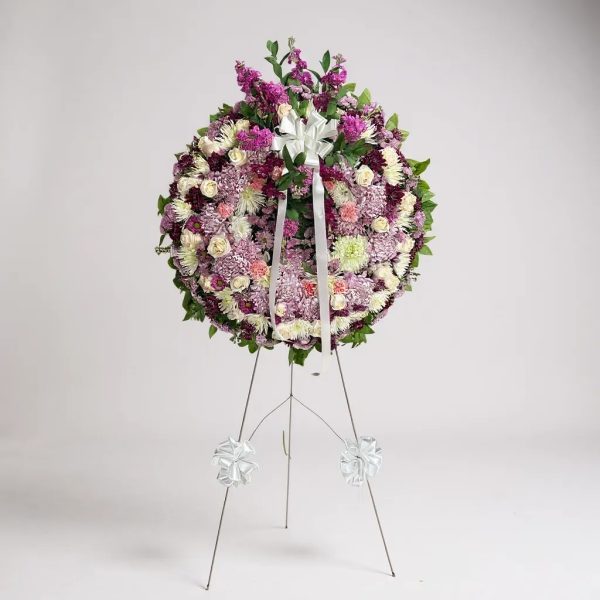 Standing funeral wreath with lavender, white, and pink flowers accented with greenery and a white bow