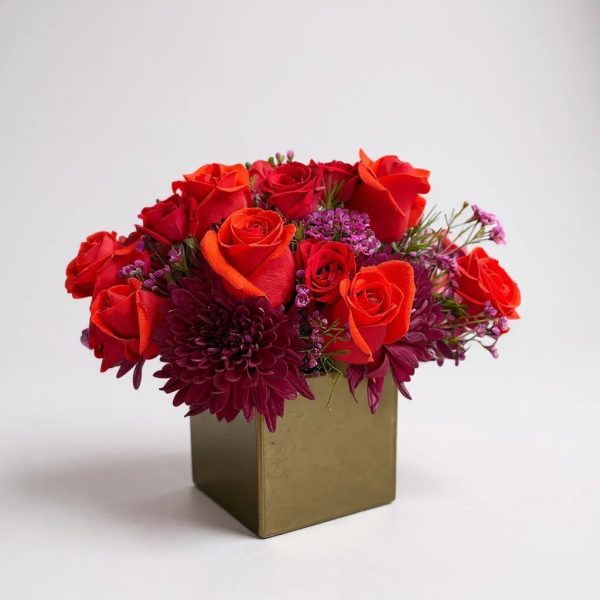 Modern cube vase arrangement with red roses, burgundy mums, and purple accent flowers