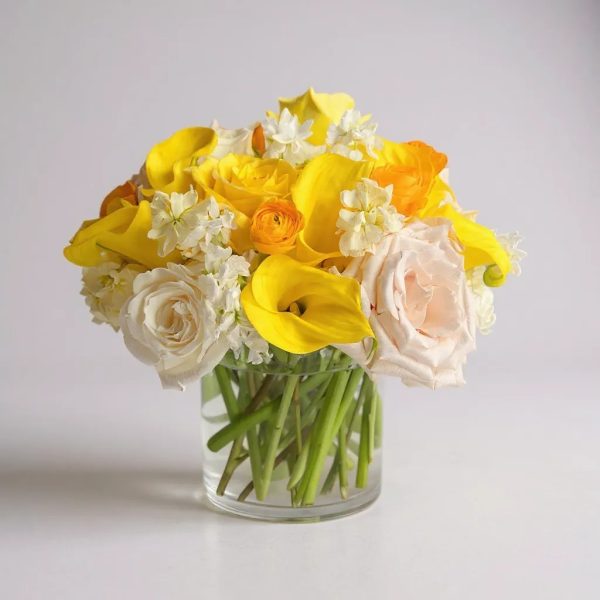 Bouquet with yellow calla lilies, white roses, orange ranunculus, and seasonal blooms in a glass vase