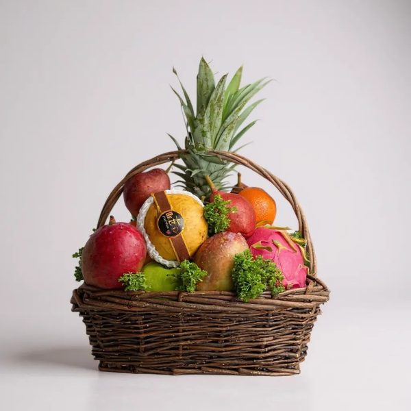 Fresh fruit basket with pineapple, apples, pears, oranges, mango, dragon fruit, and pomegranate in a wicker basket