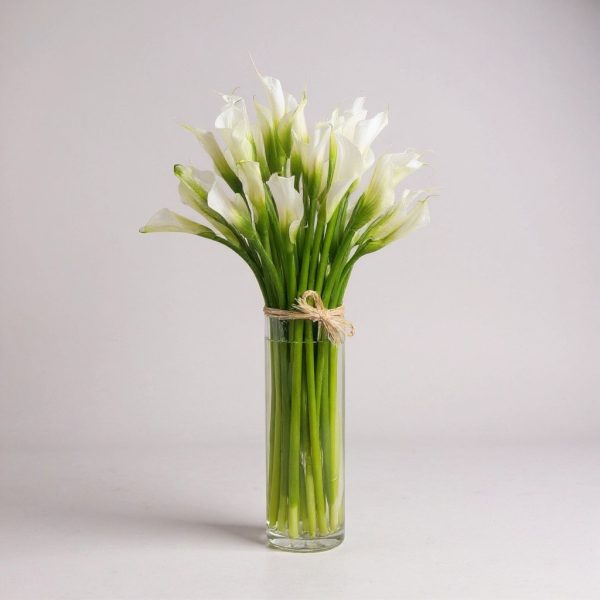 Elegant white calla lily arrangement in a clear tall glass vase with raffia tie