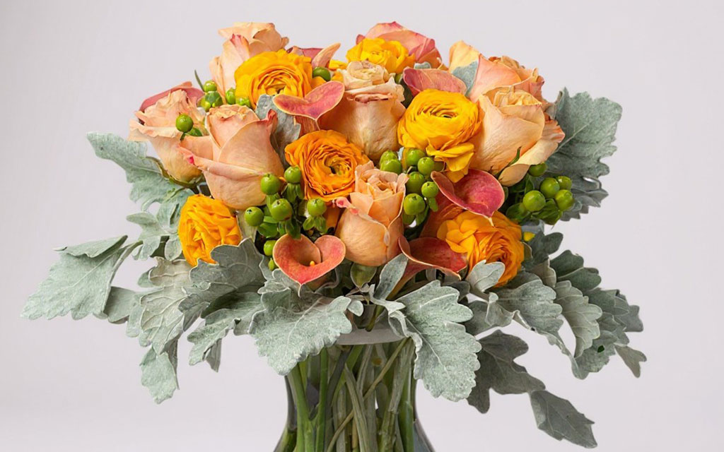 Fall wedding flowers bouquet with orange ranunculus, peach roses, green hypericum berries, and silvery dusty miller foliage