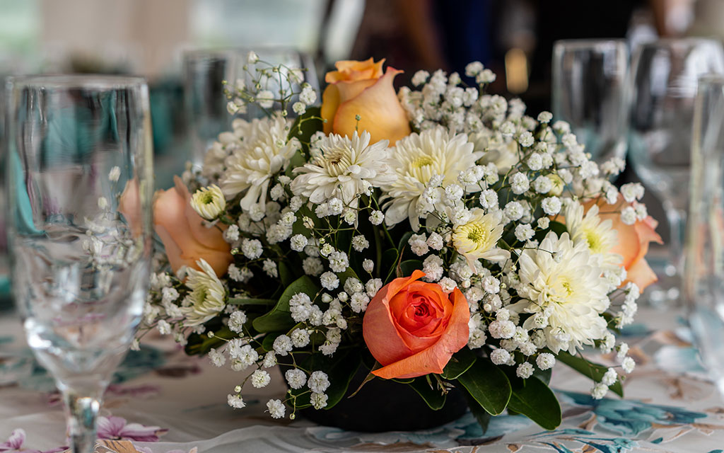 Fall wedding flowers centerpiece featuring orange roses, white chrysanthemums, and baby's breath on reception table with wine glasses