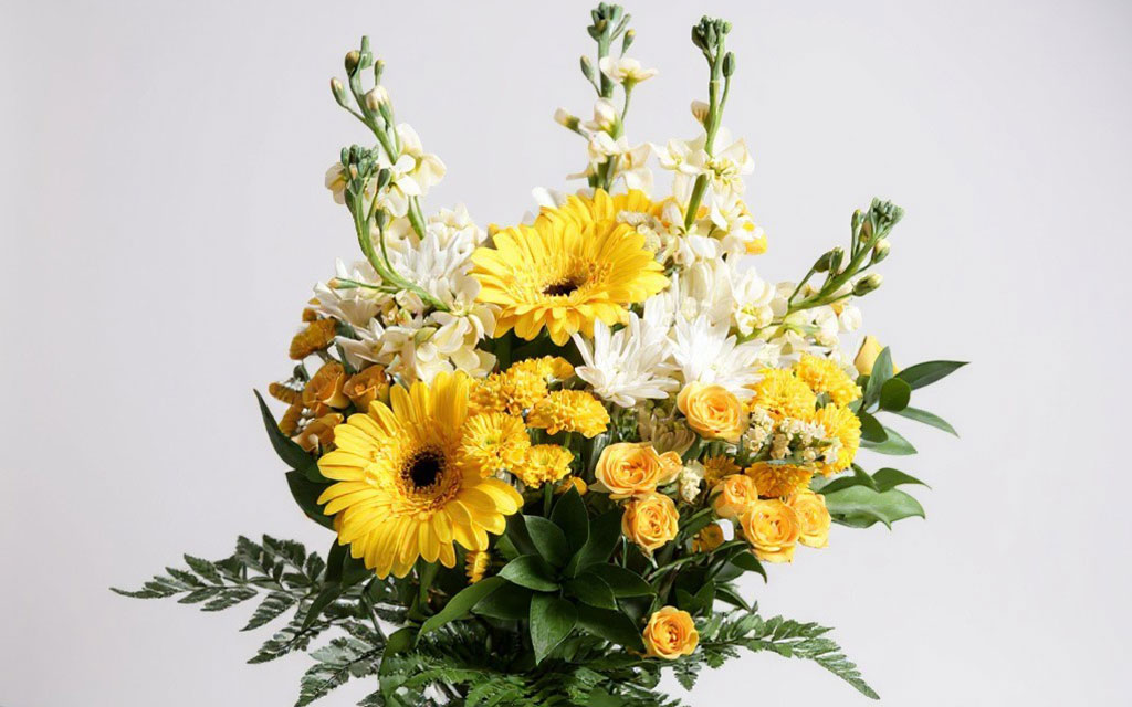 Fall wedding flowers arrangement with yellow gerbera daisies, white chrysanthemums, yellow spray roses, stock flowers, and green ferns