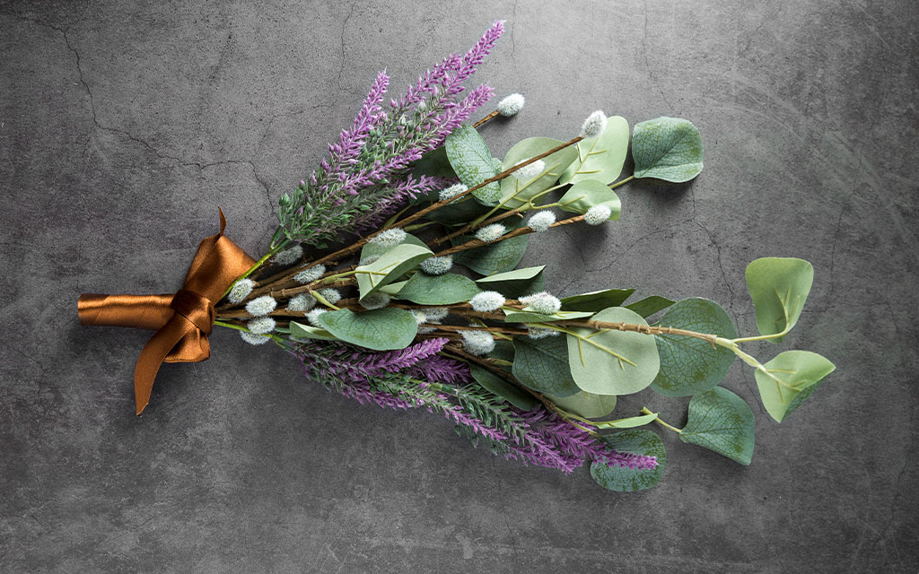 Winter wedding flowers bouquet featuring silver brunia, eucalyptus leaves, and purple heather wrapped in copper ribbon on gray background