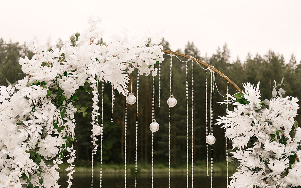 Winter wedding flowers ceremony arch with white blooms and hanging crystal strands creating winter wonderland outdoor ceremony backdrop