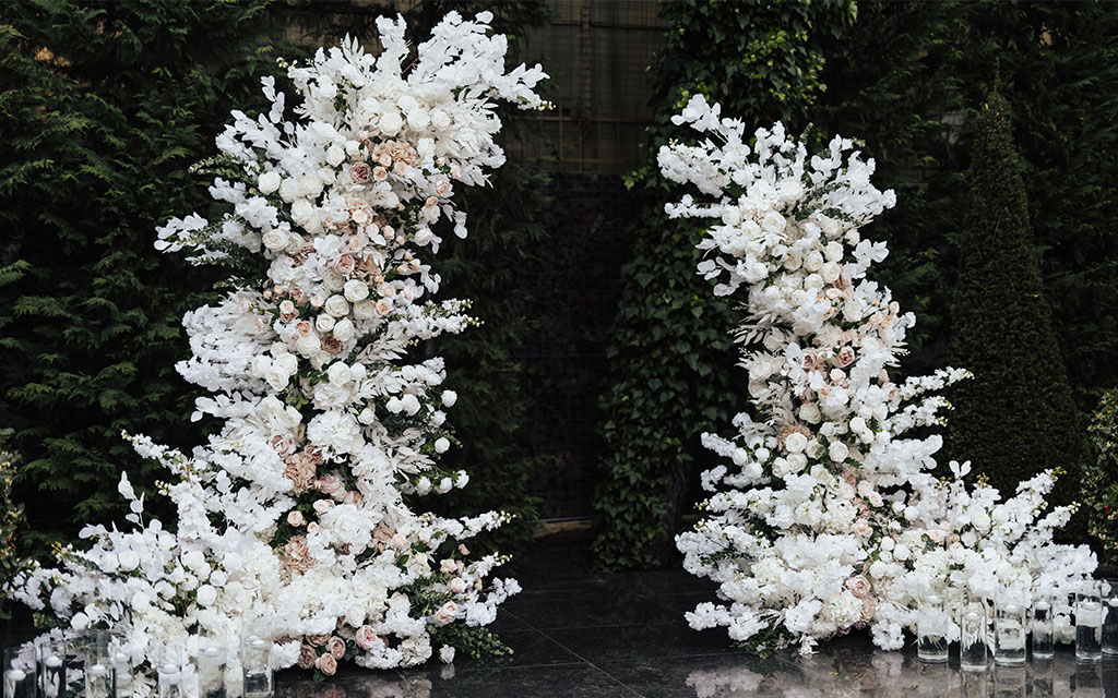 Dramatic winter wedding flowers ceremony installation with tall white orchid and rose columns flanking entrance for luxury winter celebration