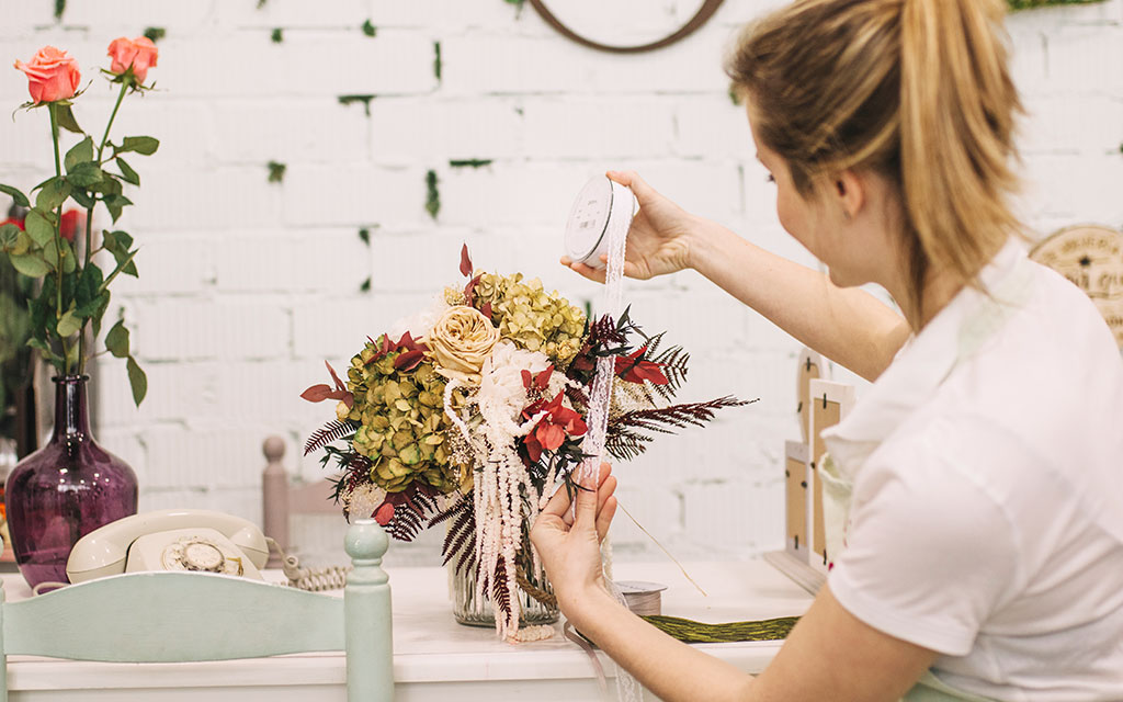 Professional florist designing winter wedding flowers arrangement with hydrangeas, amaranth, and ferns during bridal consultation